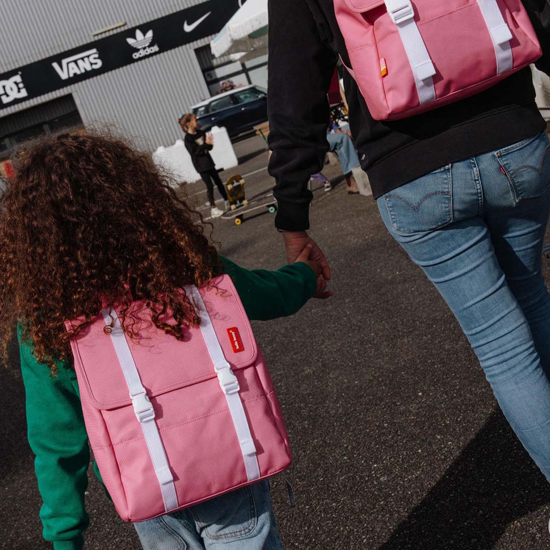 Een kind en een volwassene lopen hand in hand en dragen de hello hossy roze schoolrugzakken.