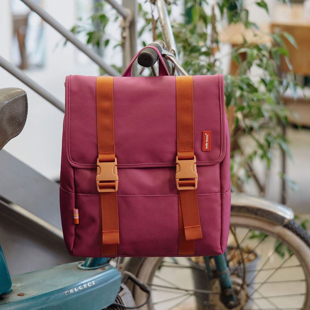 De paarse hello hossy schoolrugzak hangt aan het stuur van een fiets.