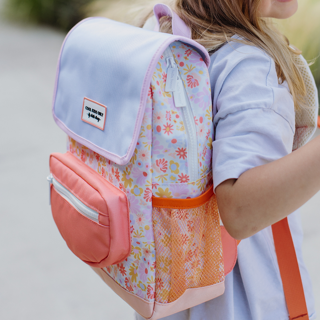 Kind draagt de Hello Hossy schoolrugzak met retro bloemenpatroon en lichtpaarse flap, buiten lopend.
