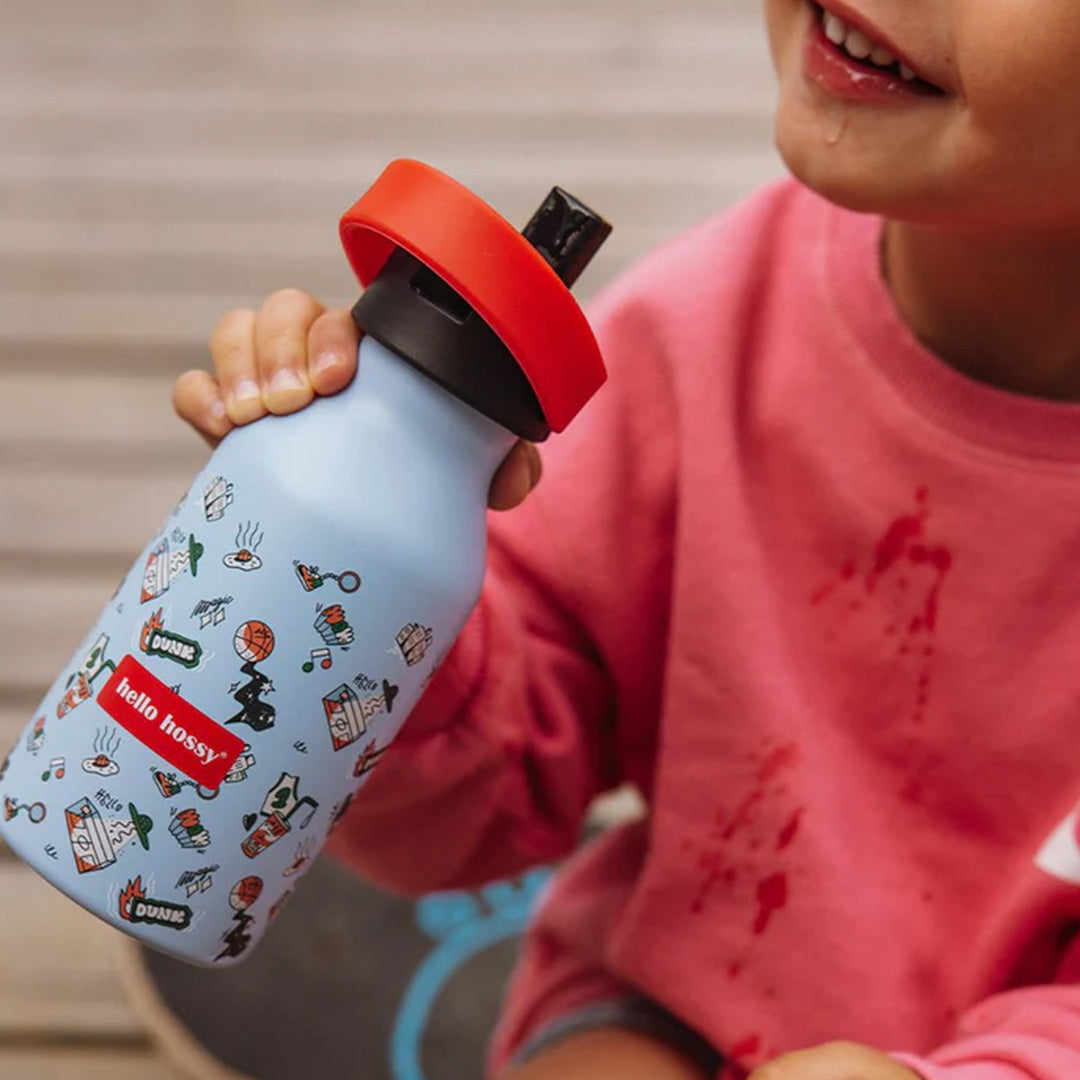 Een kind houdt de Hello Hossy blauwe thermosfles met figuren en tekst vast aan de rode handgreep.