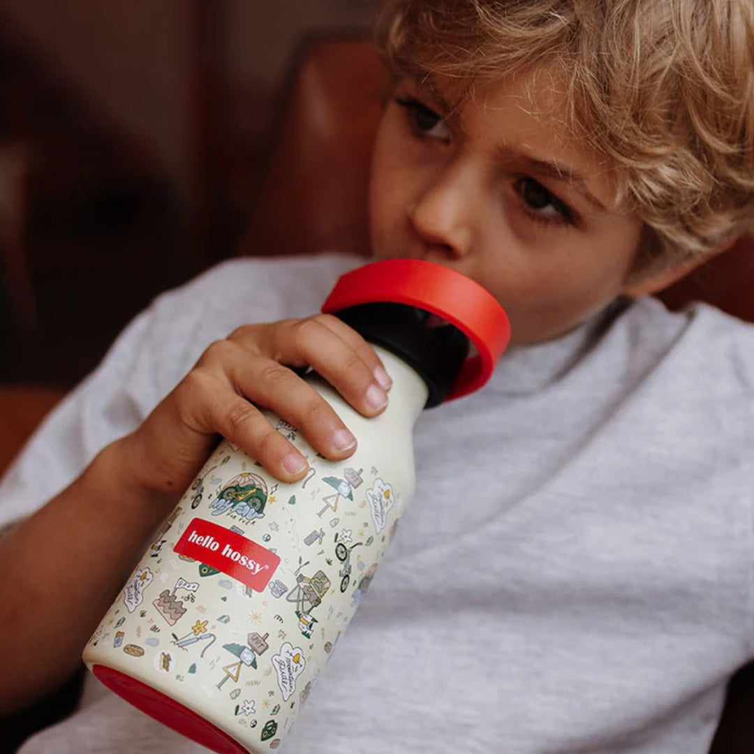 Een kind drinkt uit de beige Hello Hossy thermosfles met mountain ride figuren.