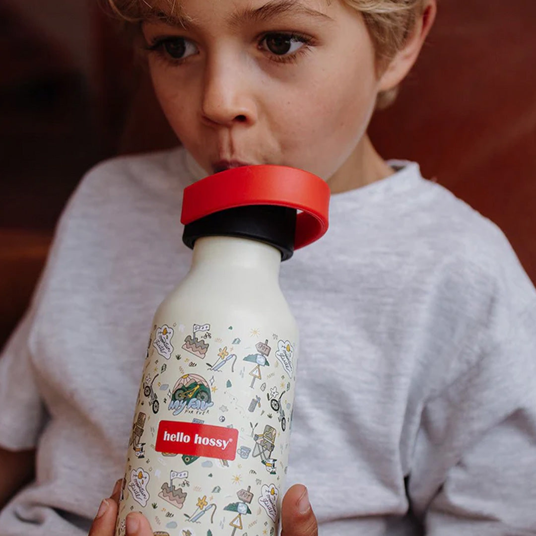 Een kind drinkt uit de beige Hello Hossy thermosfles met mountain ride figuren.