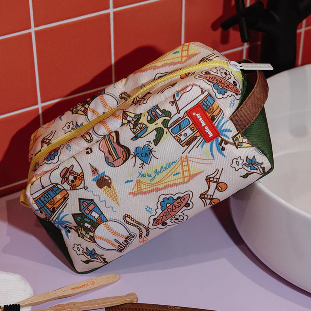 hello hossy toilettas met San Francisco thema staand op een badkamerplank naast een wasbak.