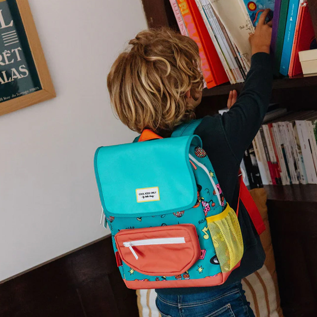 Kind met Hello Hossy schoolrugzak met disco roar patroon pakt een boek uit de kast.