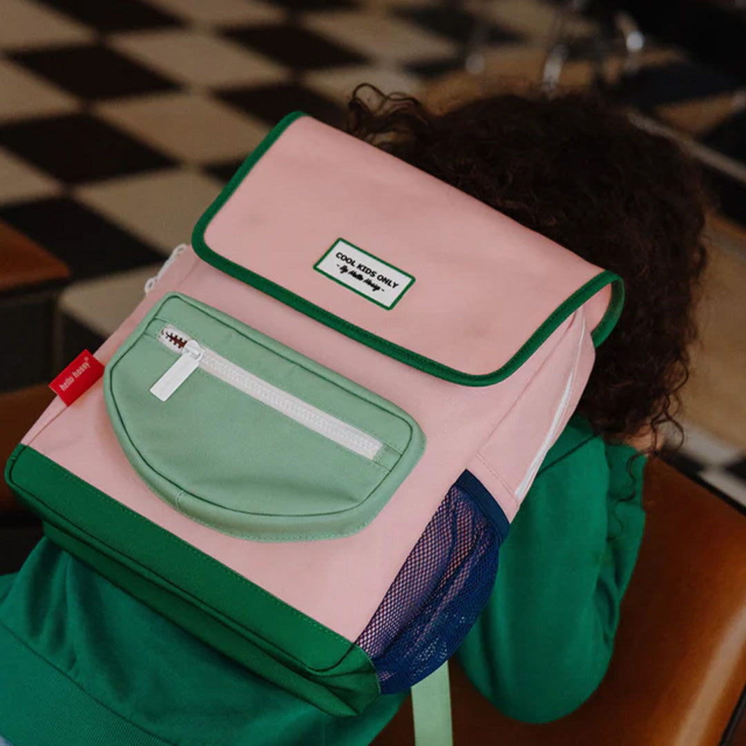 Hello Hossy kleuterrugzak in roze en groen gedragen door een kind met krullen, schuin van achteren.