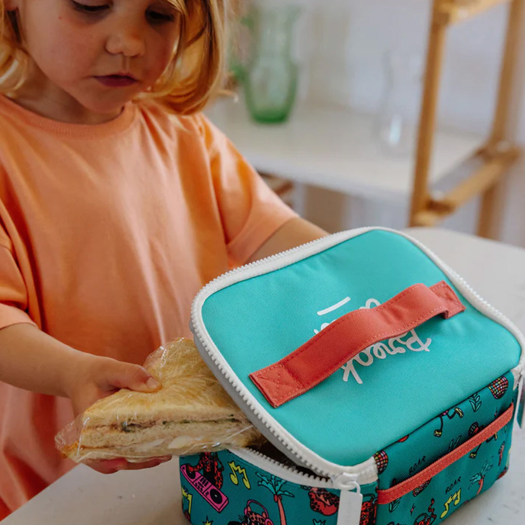 Een kind stopt een ingepakte sandwich in de open hello hossy lunchtas met disco roar patroon.