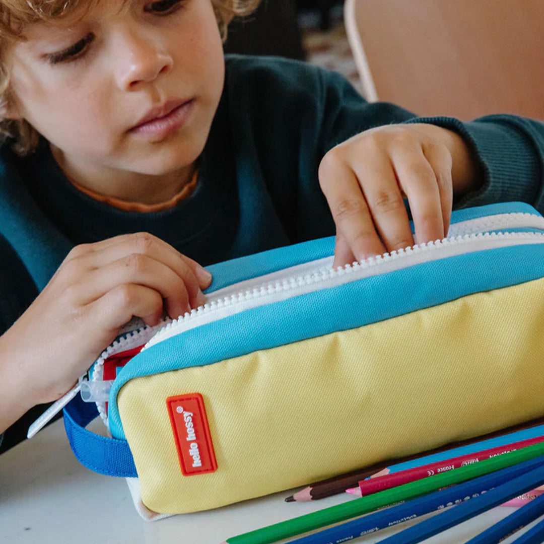 Een kind opent het hello hossy veelkleurige pennenetui met strepen, met potloden ernaast.