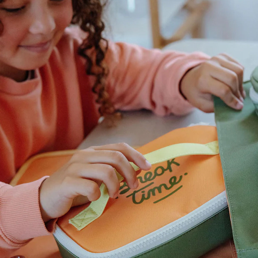 Een kind stopt de Hello Hossy mini safari snacktas in een groene rugzak.