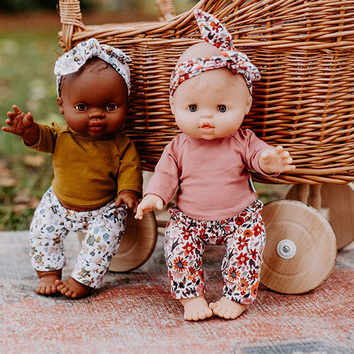 Twee poppen dragen hollie poppenkleding sets met gebloemde broeken en bijpassende haarbanden, zittend voor een rieten poppenwagen.