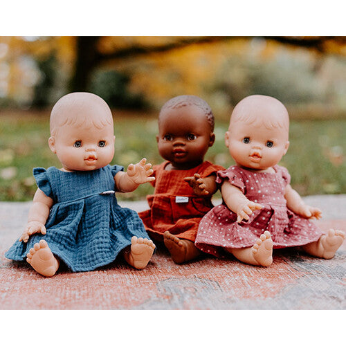 Drie baby poppen met verschillende huidskleuren dragen hollie poppenkleding jurkjes in blauw, terra en rood met stippen.