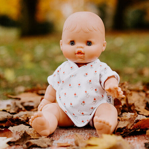 Pop met Hollie poppenkleding romper met bloemenpatroon, zittend tussen herfstbladeren.