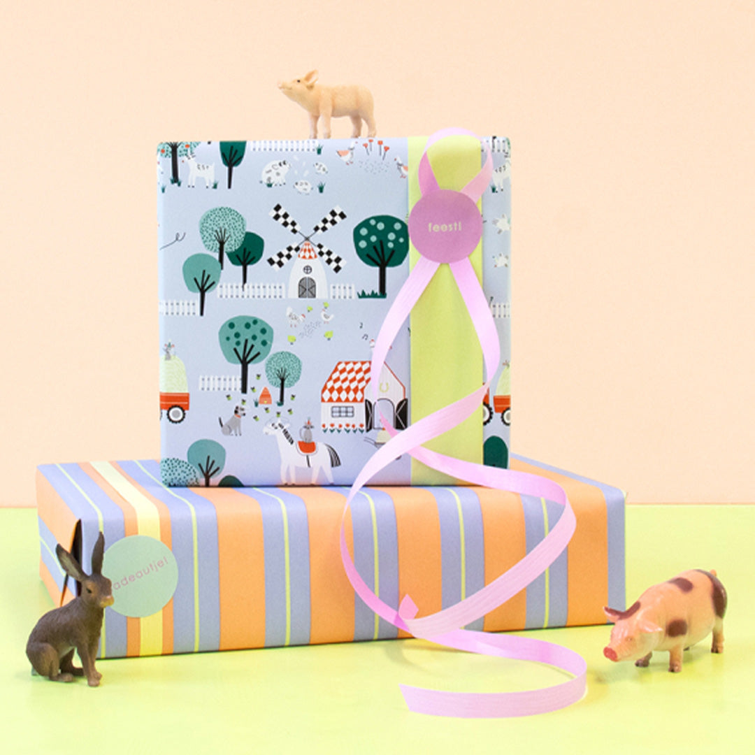 Twee ingepakte cadeaus, waarvan één met house of products inpakpapier met boerderijthema en roze lint, omringd door speelgoeddieren.