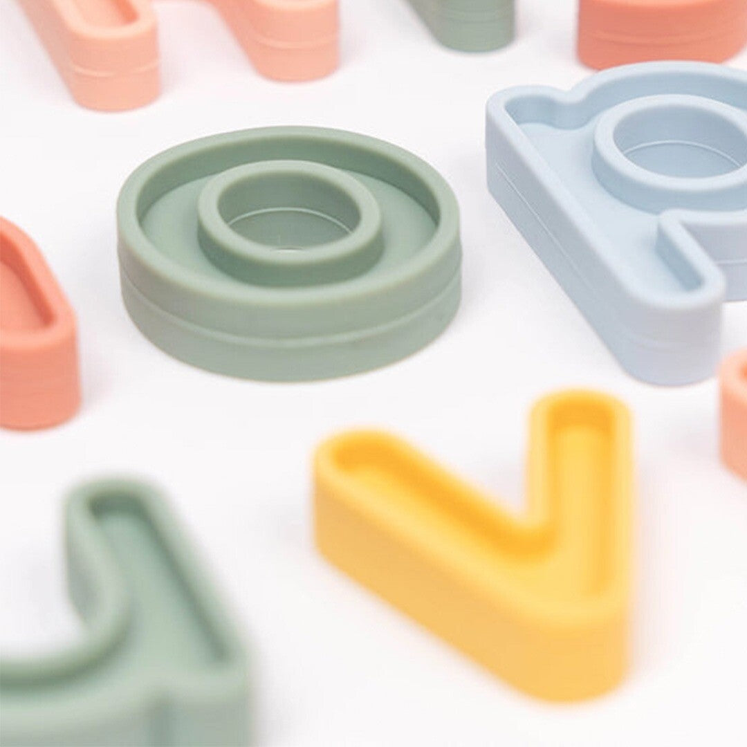 Detail van diverse pastelkleurige siliconen letters, waaronder een groene 'o' en een gele 'v', op een witte achtergrond.