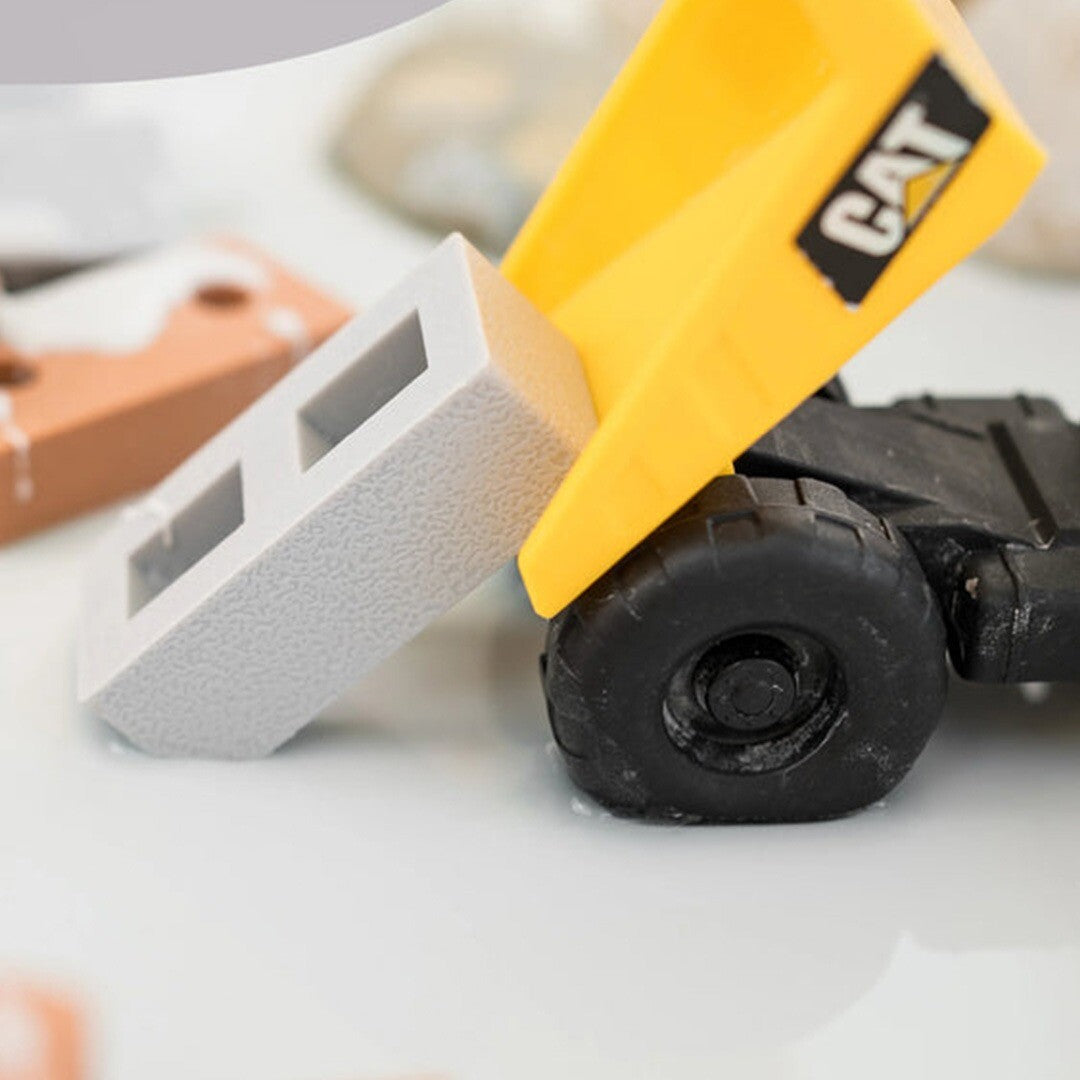 Detail van een grijs inspire my play siliconen mini blok dat uit een gele speelgoedvrachtwagen valt.