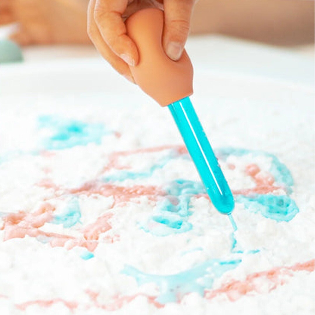 Een hand gebruikt een inspire my play pipet om blauwe vloeistof op een wit poederoppervlak te druppelen.