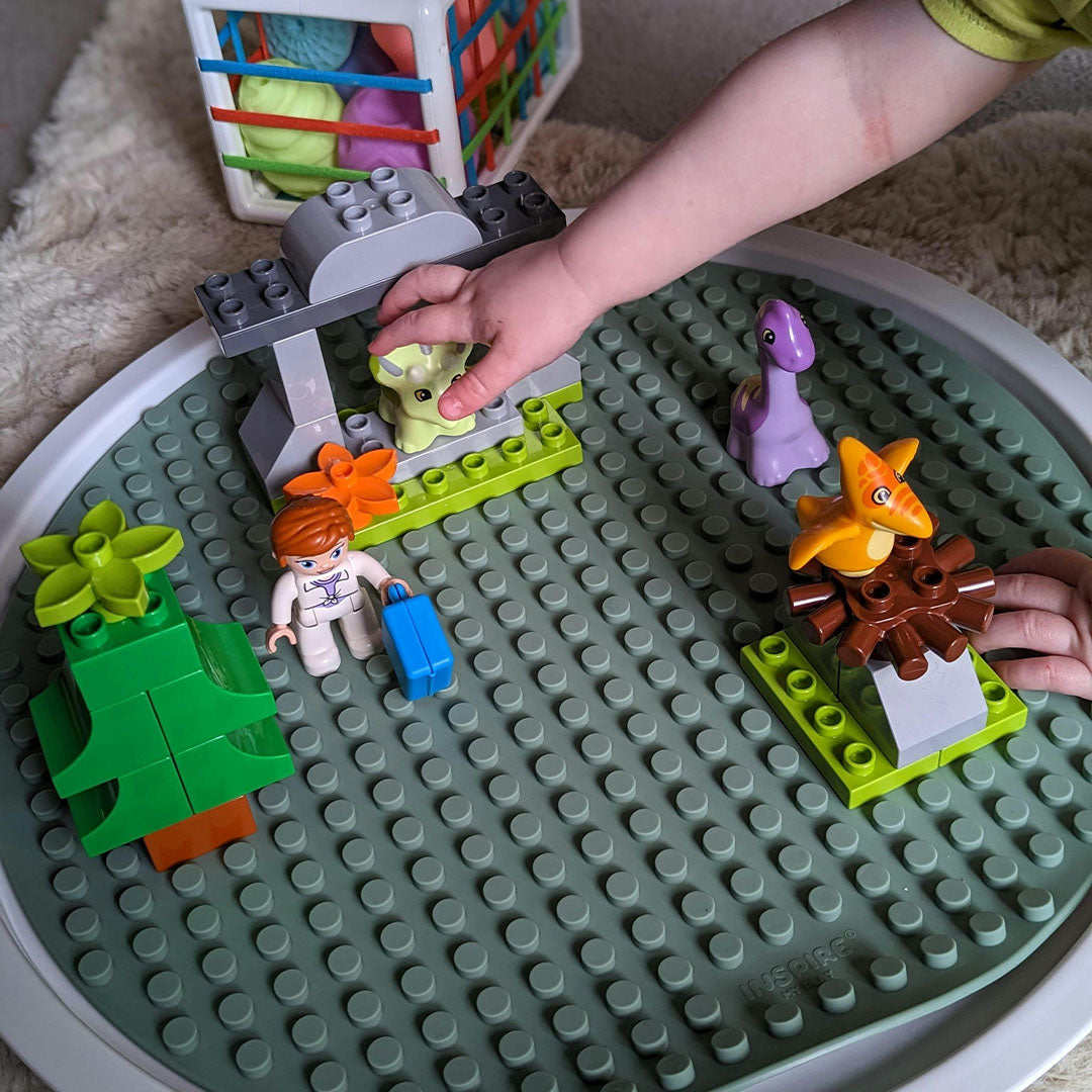 Een kind speelt met bouwblokken en dinosaurussen op de inspire my play groene bouwmat in een witte speelbak.