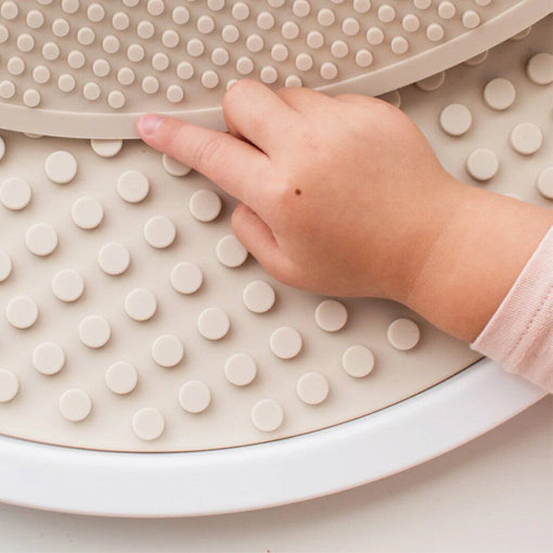 Een kinderhand raakt de beige siliconen bouwmat met noppen aan.