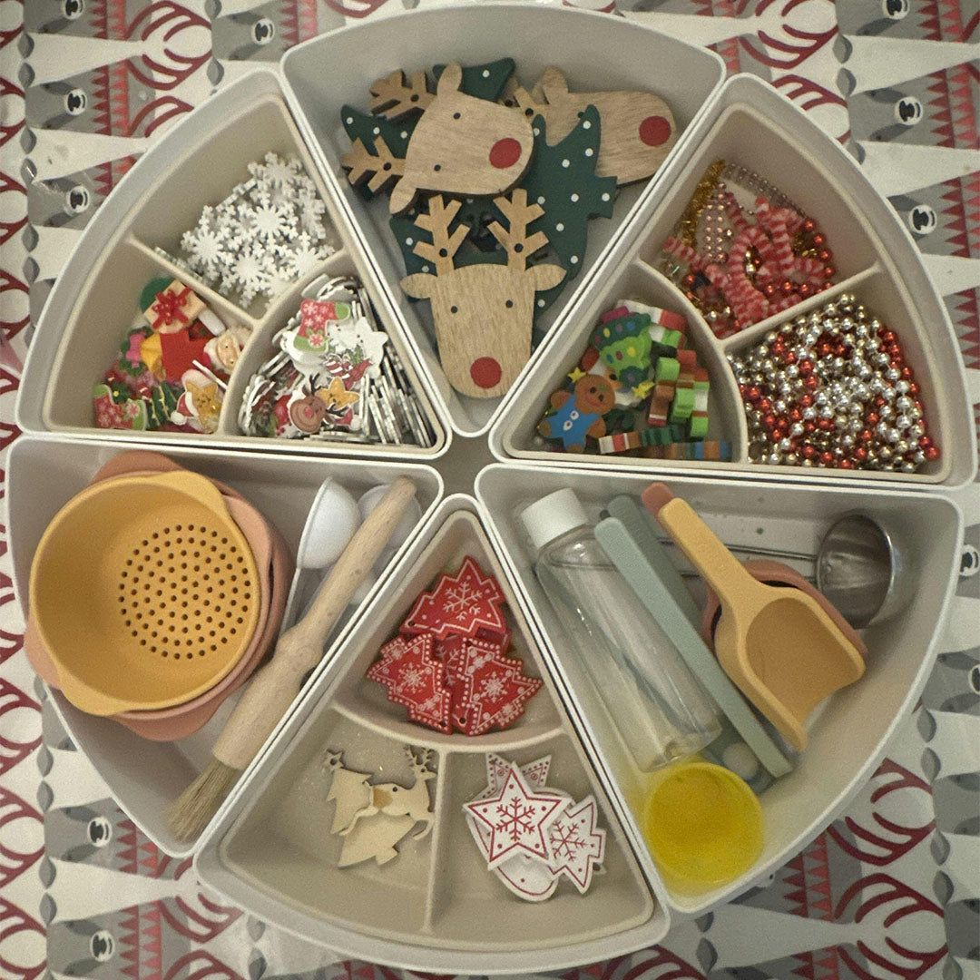 Meerdere witte playtray inserts gerangschikt in een cirkel, gevuld met diverse kerstdecoraties en sensorisch speelgoed.