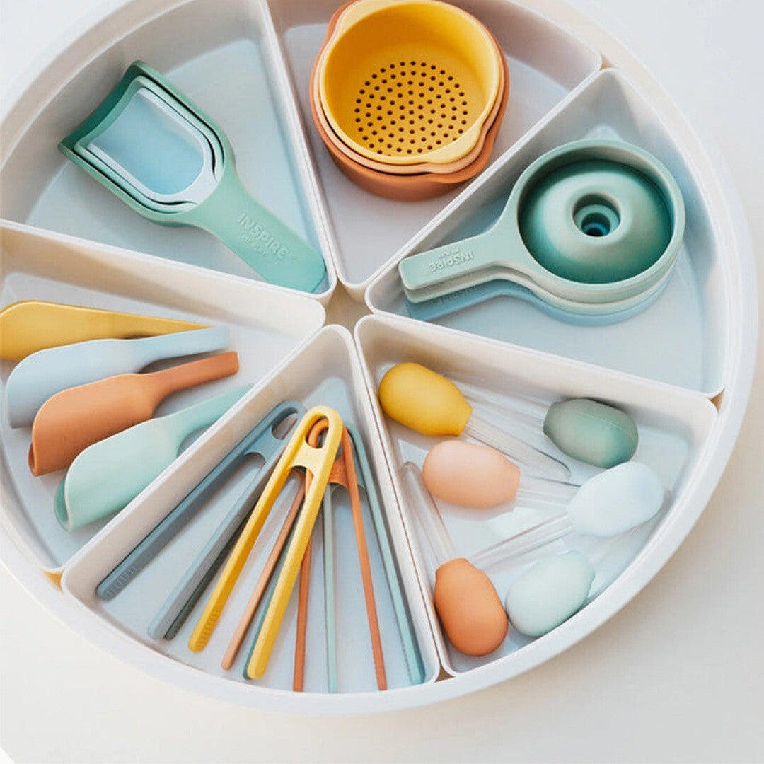 Een bovenaanzicht van een collectie inspire my play sensorisch speelgoed, waaronder tangen, schepjes en zeefjes, in een witte sorteerbak.