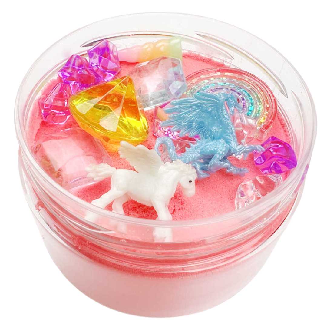 Invitation to imagine magic sand surprise pot met roze zand, een witte pegasus, blauwe draak, regenboog en edelstenen, schuin van bovenaf gezien.