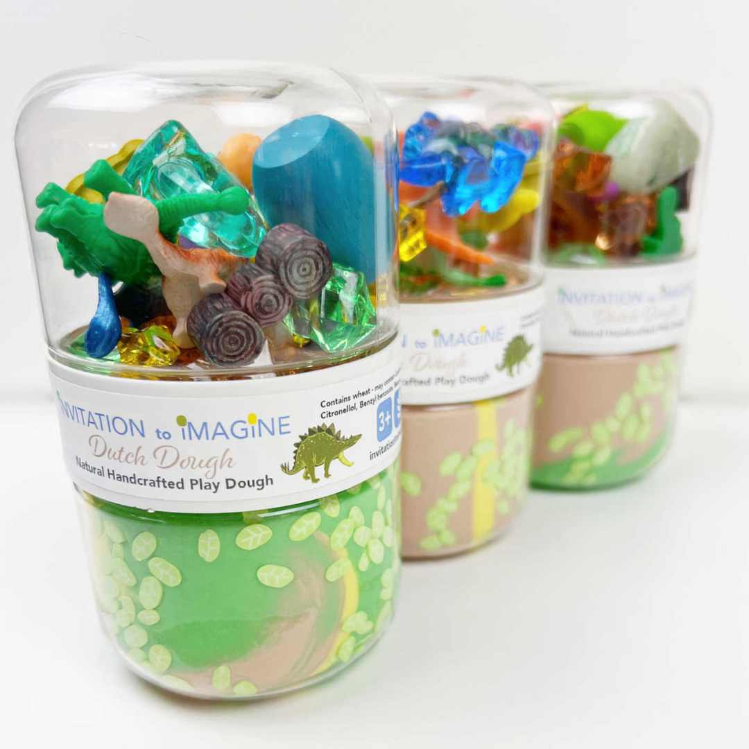 Drie invitation to imagine speelklei play pots met dinosaurus thema, schuin van voren gefotografeerd.
