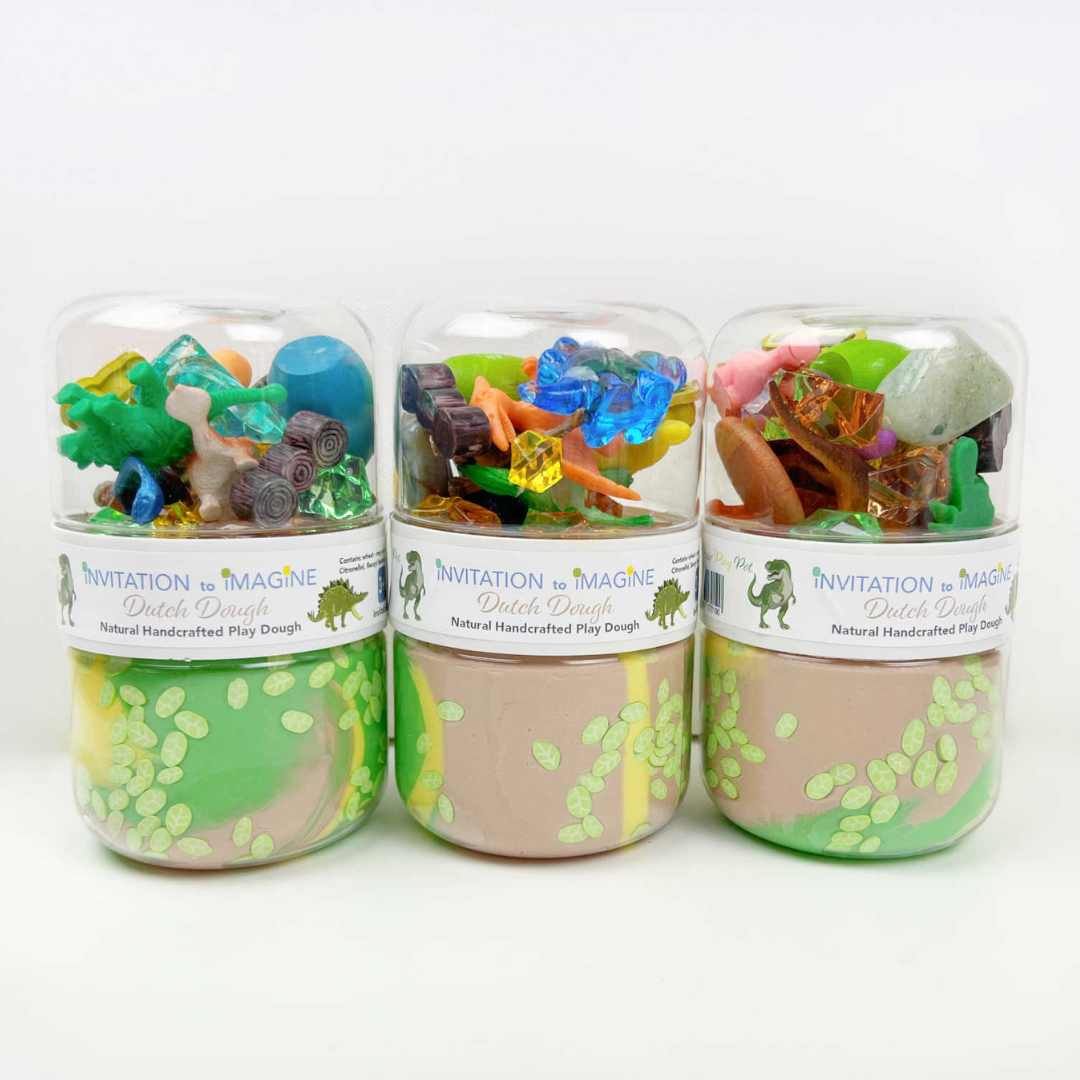 Drie invitation to imagine speelklei play pots met dinosaurus thema, van voren gefotografeerd.