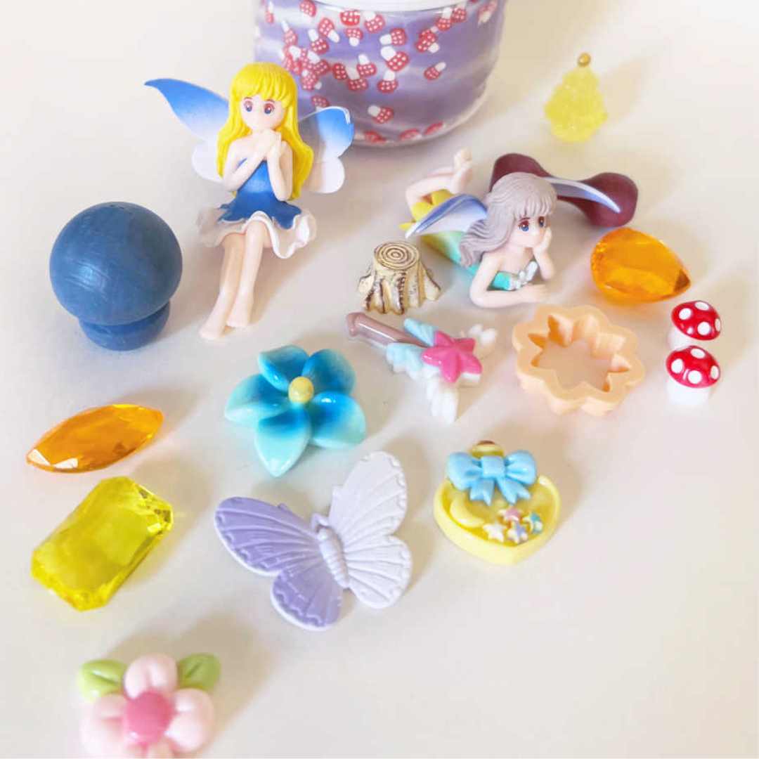 Uitgestalde accessoires van de invitation to imagine speelklei set, waaronder twee fairy figuren, bloemen, vlinders en paddenstoelen.