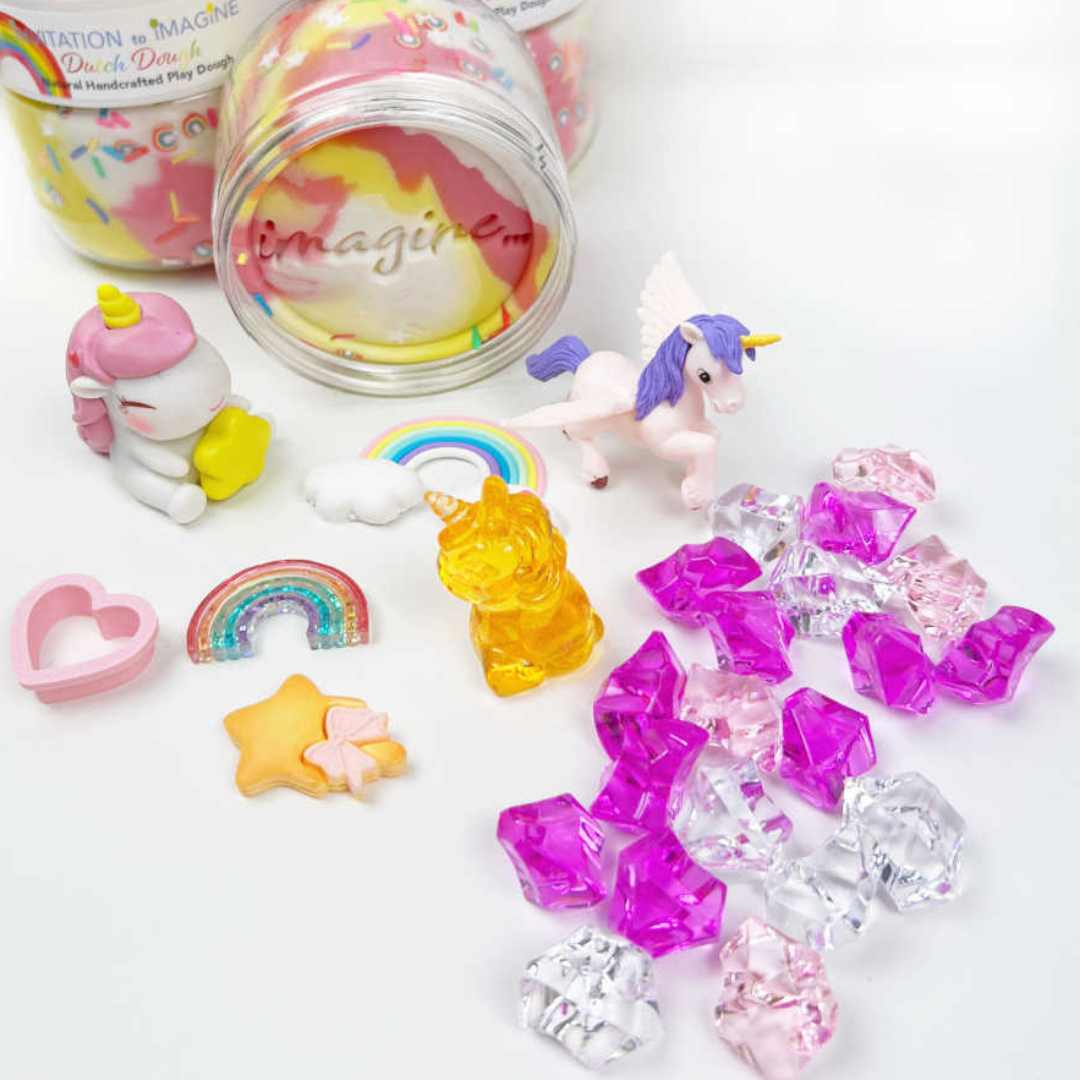 Invitation to imagine speelklei set met eenhoornfiguren, een regenboog, een hartvormige uitsteker en plastic edelstenen, uitgestald op een witte ondergrond.