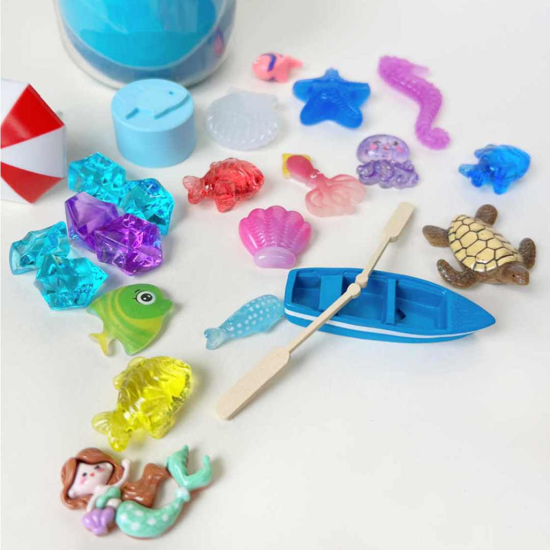Een collectie van kleine plastic en houten onderwater speelgoedfiguren, waaronder een bootje, vissen, een schildpad en een zeemeermin.