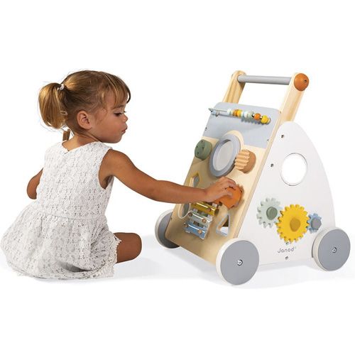 Een jong meisje speelt zittend met de draaiende tandwielen van de Janod activiteitentrolley.