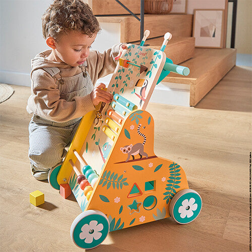 Een peuter speelt zittend op de grond met de Janod houten loopwagen met jungle thema.