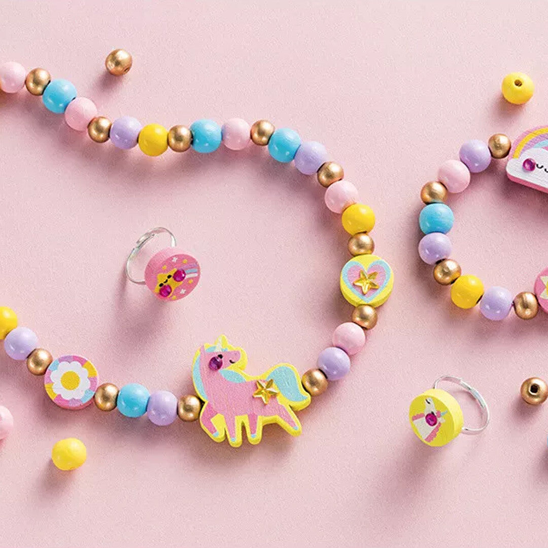 Detailfoto van Janod houten sieraden met een eenhoorn, regenboog en pastelkleurige kralen op een roze achtergrond.