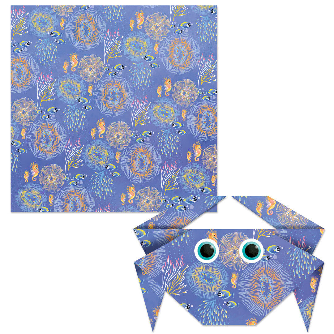 Een vel origami papier met zeedierenpatroon en een gevouwen krab met ogen uit de Janod Magic Ocean knutselset.