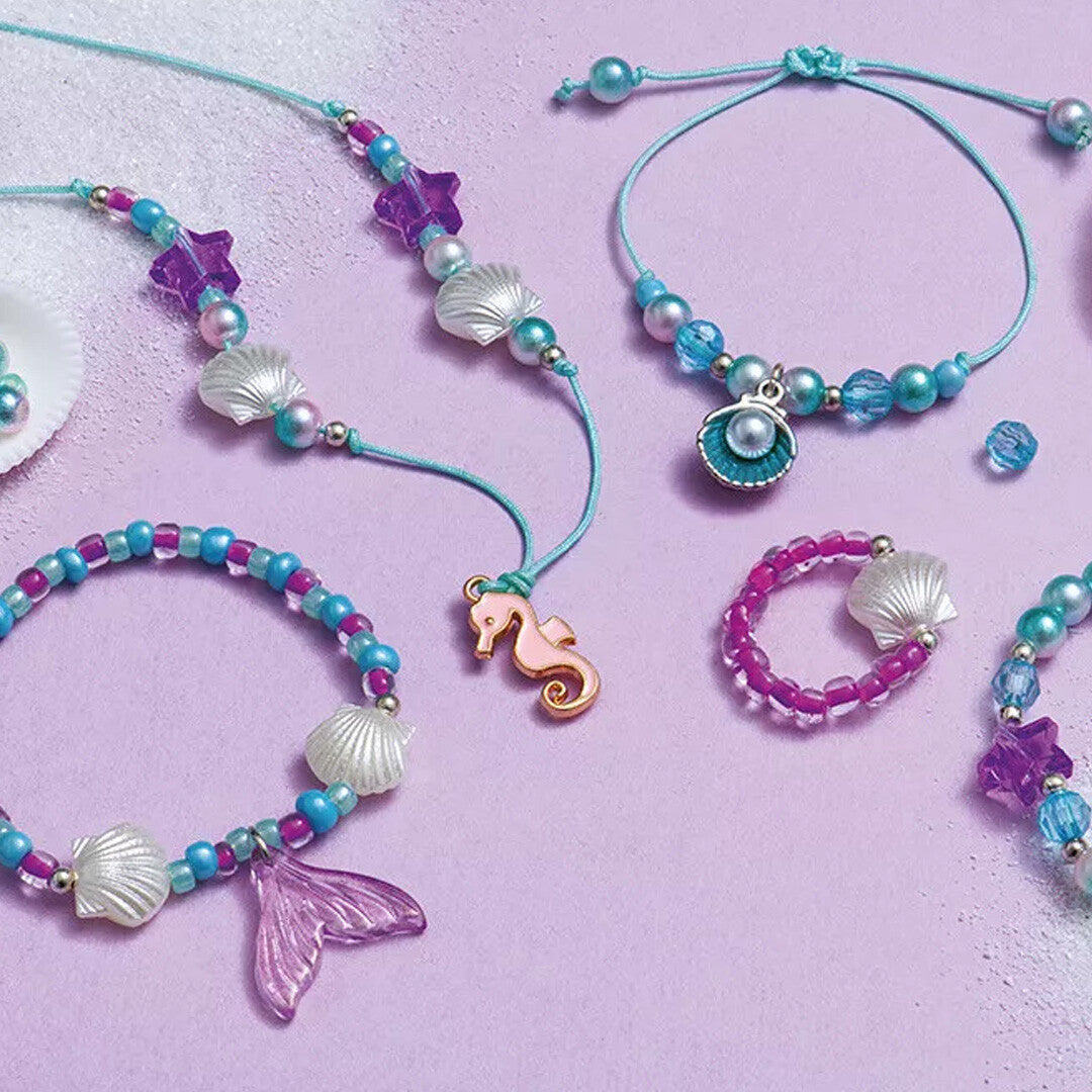 Detail van diverse gemaakte sieraden met zeethema, zoals armbanden, ringen en een ketting met schelpen en een zeepaardje.