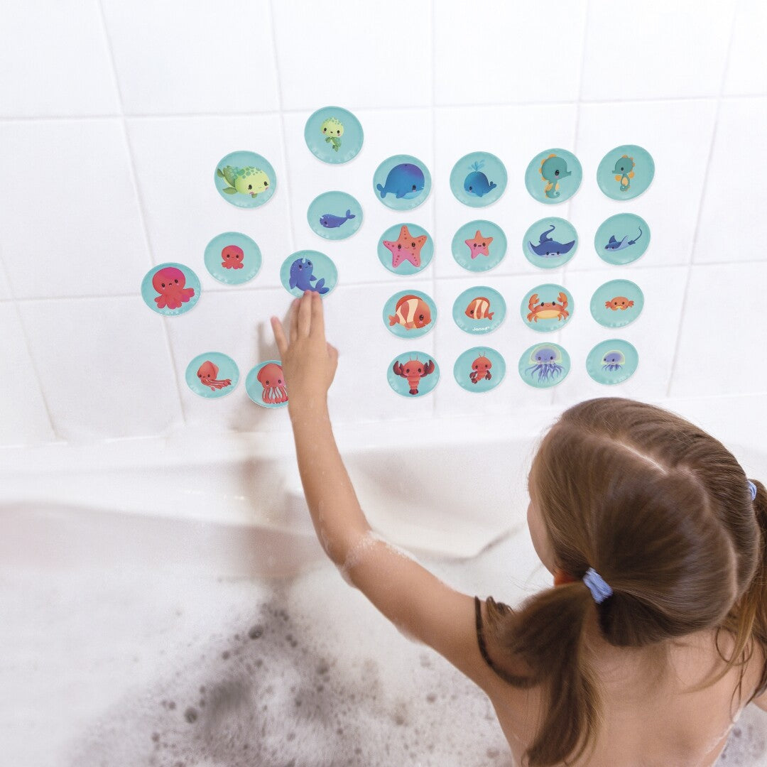 Een kind in bad plakt de ronde Janod badspel memorie speelstukken met babydieren op de badwand.
