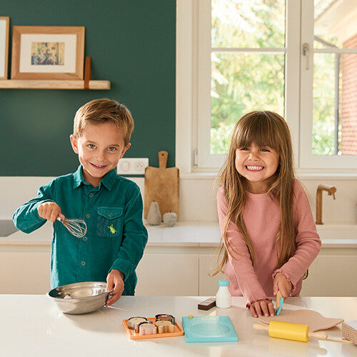 Twee lachende kinderen spelen in een keuken met de Janod speelgoed bakset.