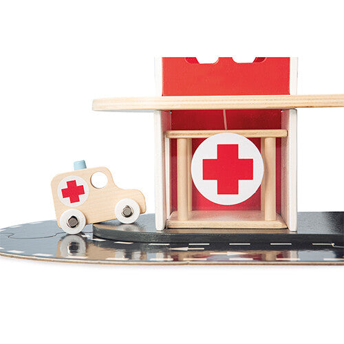 Detail van de Janod houten brandweerkazerne speelset met een ambulance naast de ingang met rood kruis.