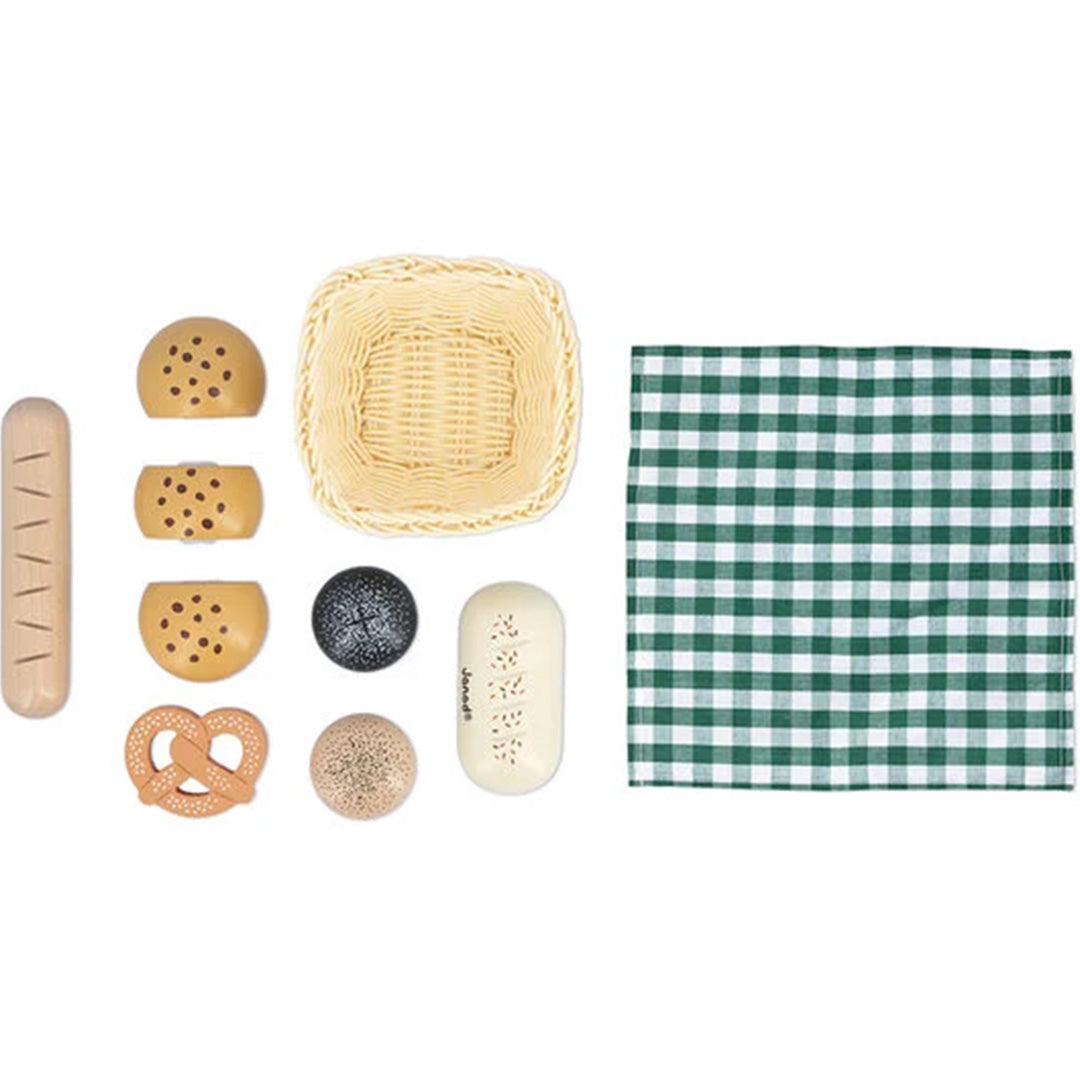 Janod houten speelgoed broodmandje, geruite doek en alle losse speelgoedbroodjes en pretzels plat op een witte ondergrond.
