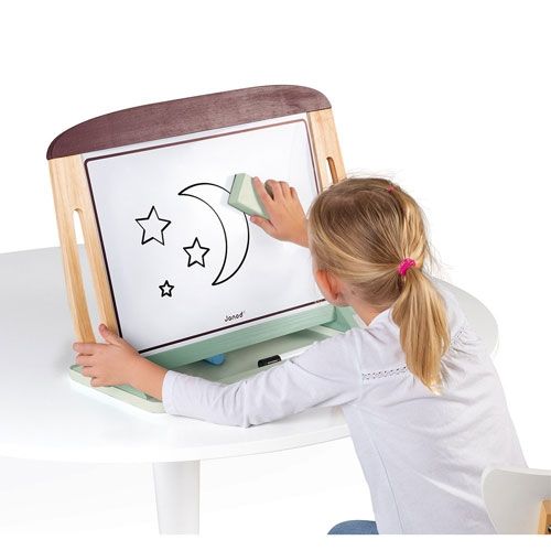 Een meisje wist een tekening van een maan en sterren van het Janod draagbare whiteboard, staand op een witte tafel.