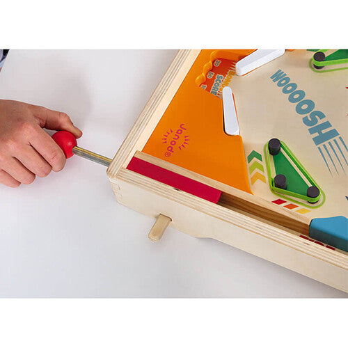 Een hand trekt aan de rode lanceerknop van de Janod houten flipperkast.