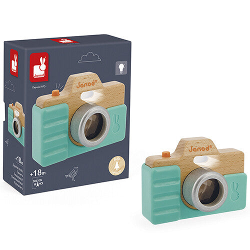 De Janod houten speelgoedcamera met caleidoscoop en flits naast de donkerblauwe productverpakking.