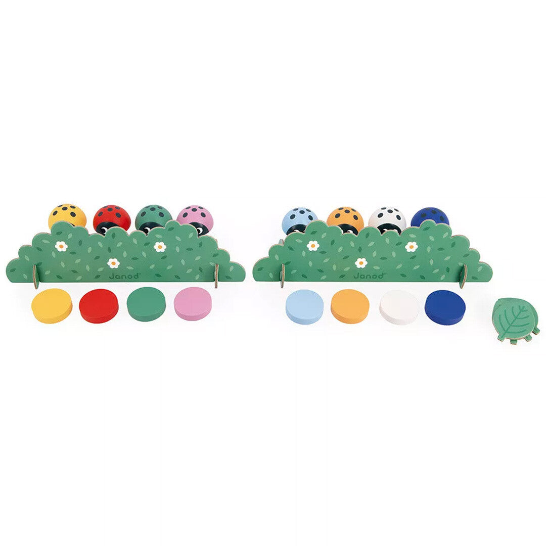 Twee opstellingen van het Janod houten geheugenspel met lieveheersbeestjes achter groene struiken en gekleurde schijven.