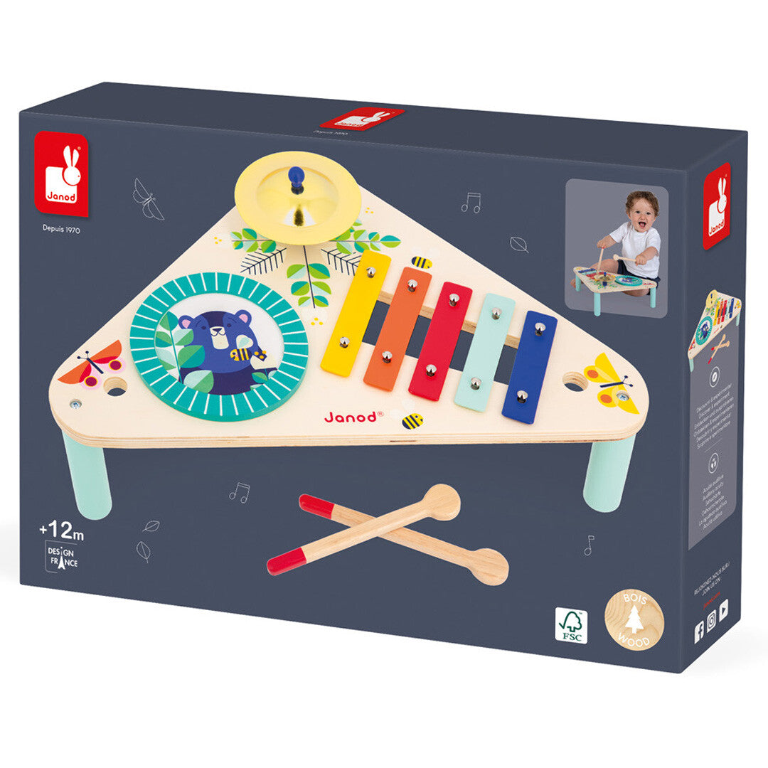 De verpakking van de Janod Gioia houten muziektafel, met een afbeelding van het speelgoed en een spelend kind.