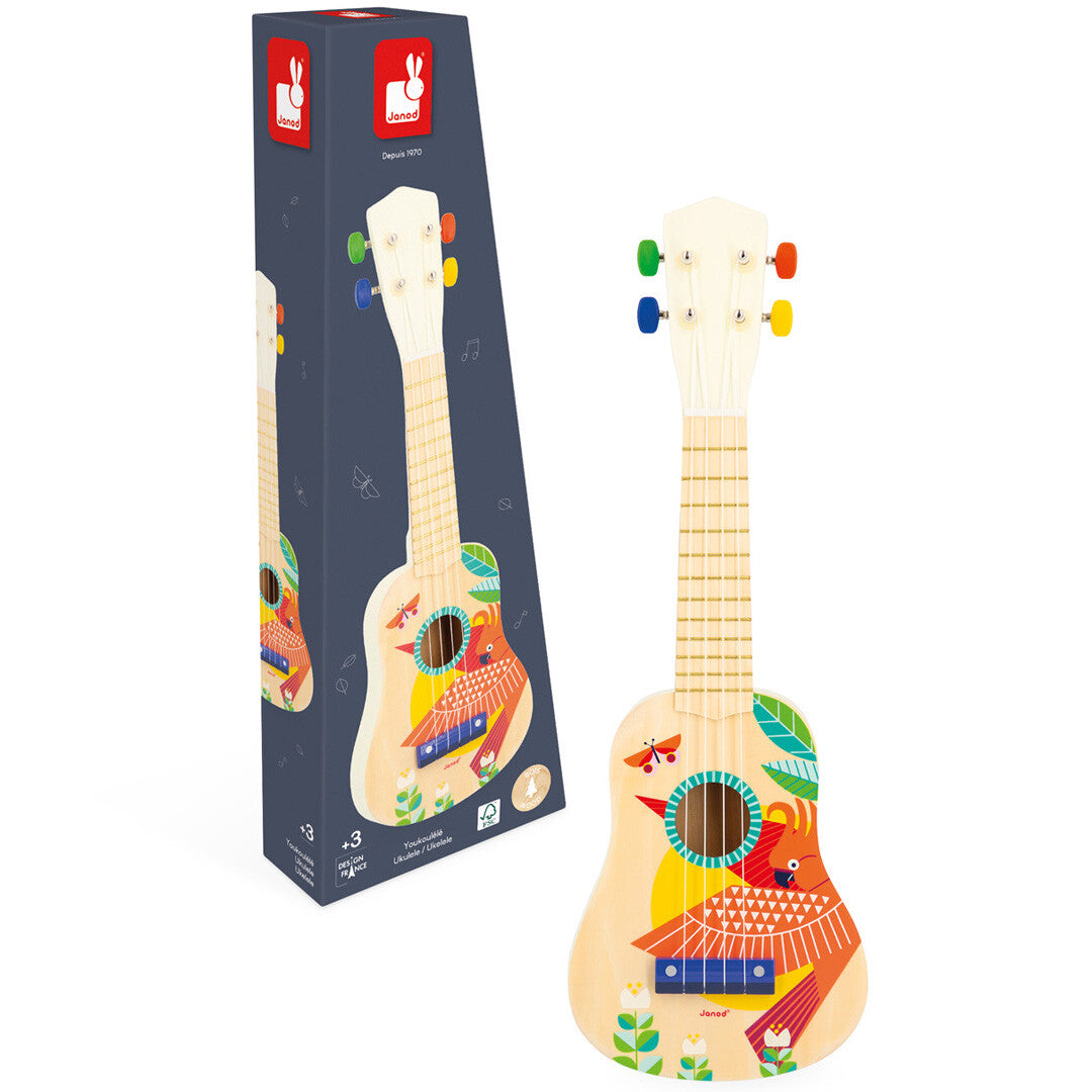 Janod houten kinderukelele met vogelprint naast de productverpakking, beide schuin gefotografeerd.