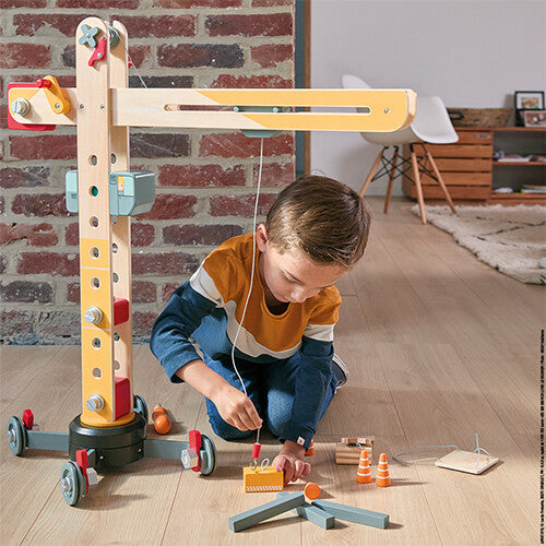 Een jongen speelt met de Janod houten hijskraan en gebruikt de speelgoedschroevendraaier.