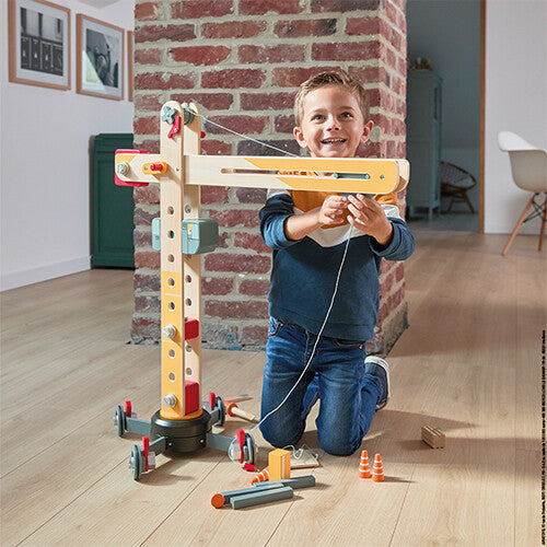 Een lachende jongen speelt met de Janod houten hijskraan in een woonkamer.