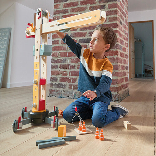 Een jongen speelt met de Janod houten hijskraan en bedient de takel om objecten te verplaatsen.