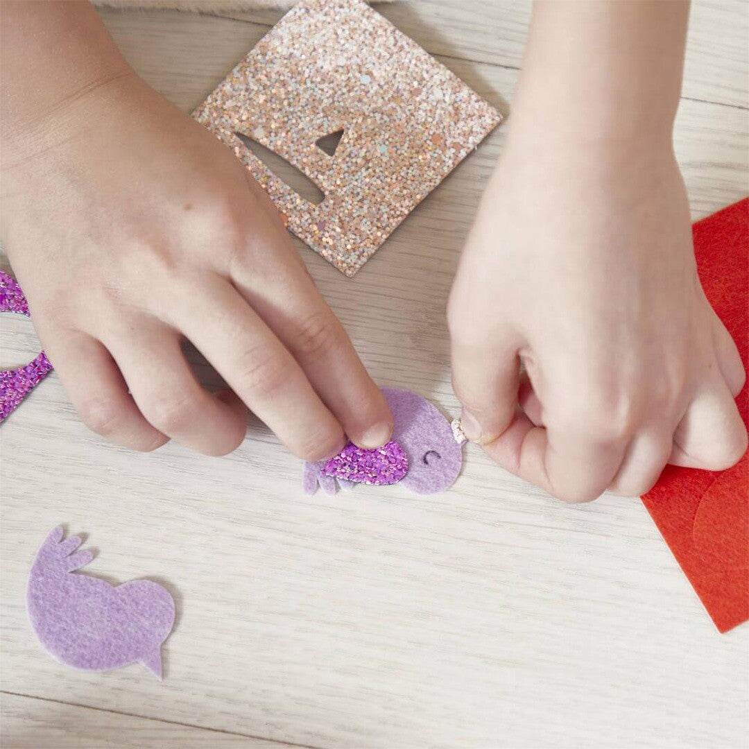 Kinderhanden knutselen een paars konijn haarclipje van vilt en glittermateriaal.
