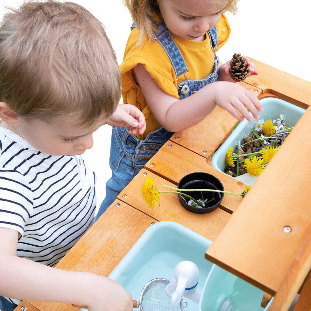 Detail van twee kinderen die met bloemen en een zeef spelen in de Janod modderkeuken.
