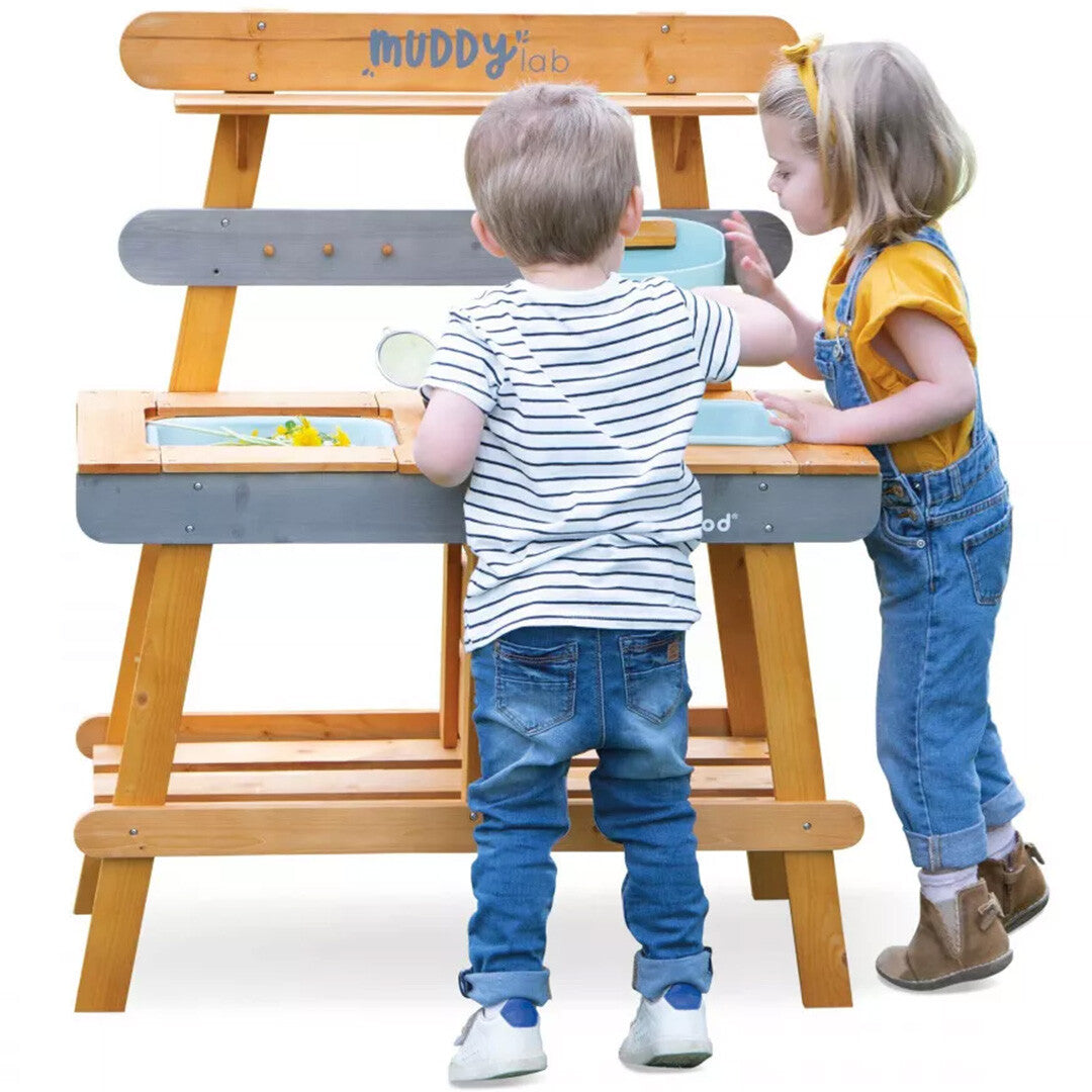 Twee kinderen spelen aan de achterkant van de Janod houten modderkeuken.